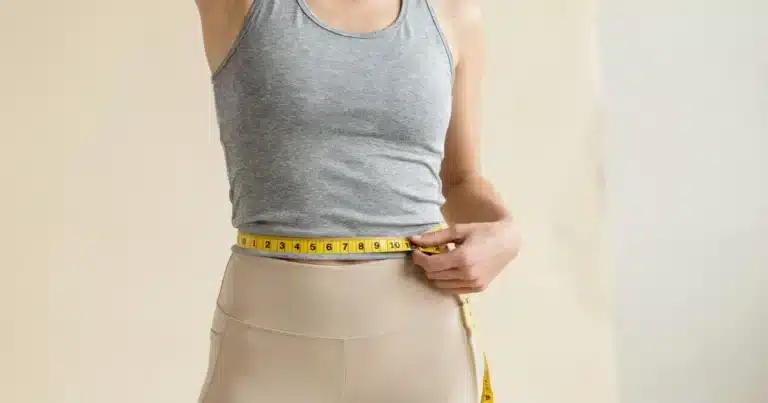 Person measuring waist with a tape measure to track fat loss progress