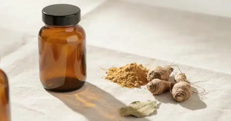 Maca root powder in a bowl with a wooden spoon and capsules