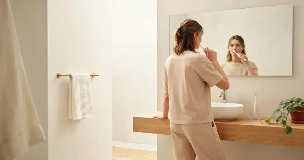 Person brushing their teeth at a bathroom mirror as part of a daily oral hygiene routine